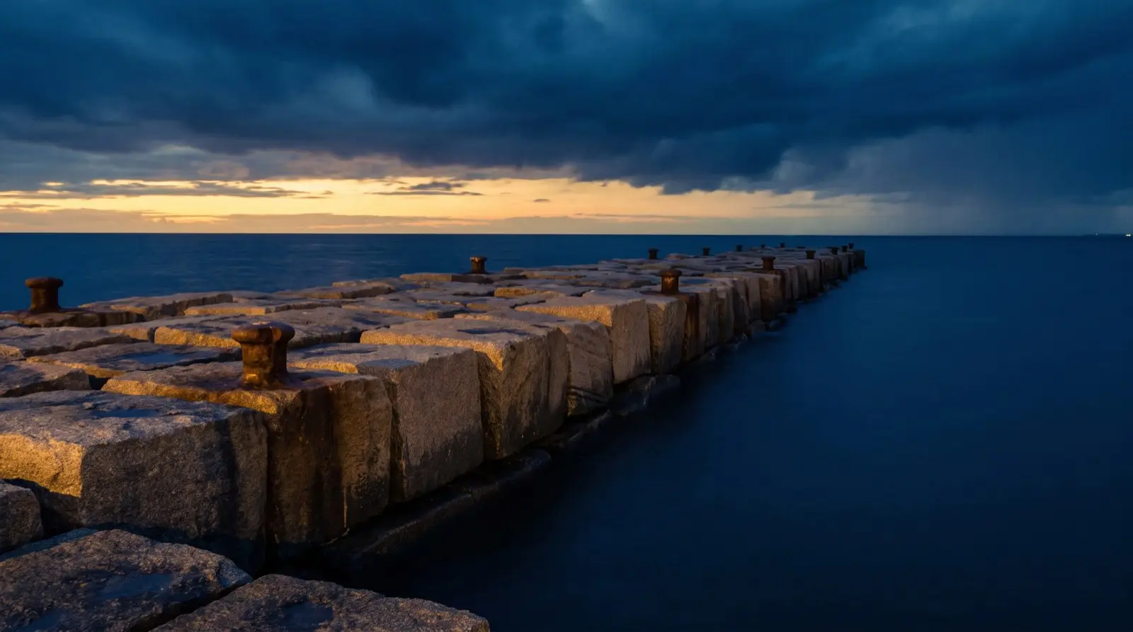 A granite harbor breakwater running into deep calm water at blue hour